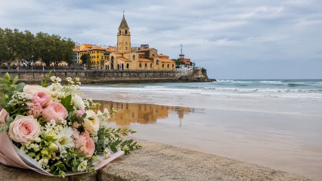 Ramo de flores rosas frente a la playa de San Lorenzo y la Iglesia de San Pedro en Gijón